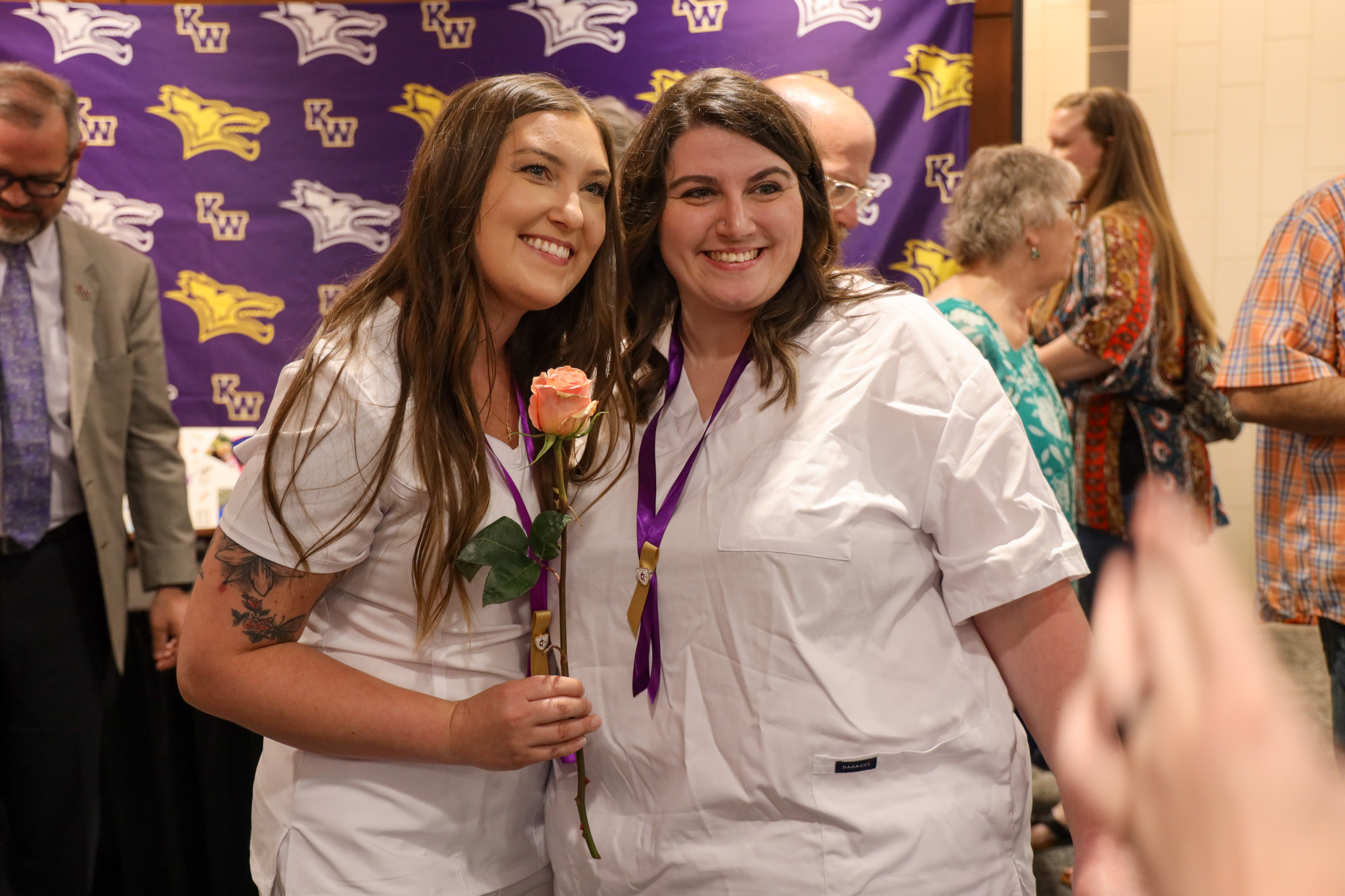 Two female nursing graduates together, one with rose