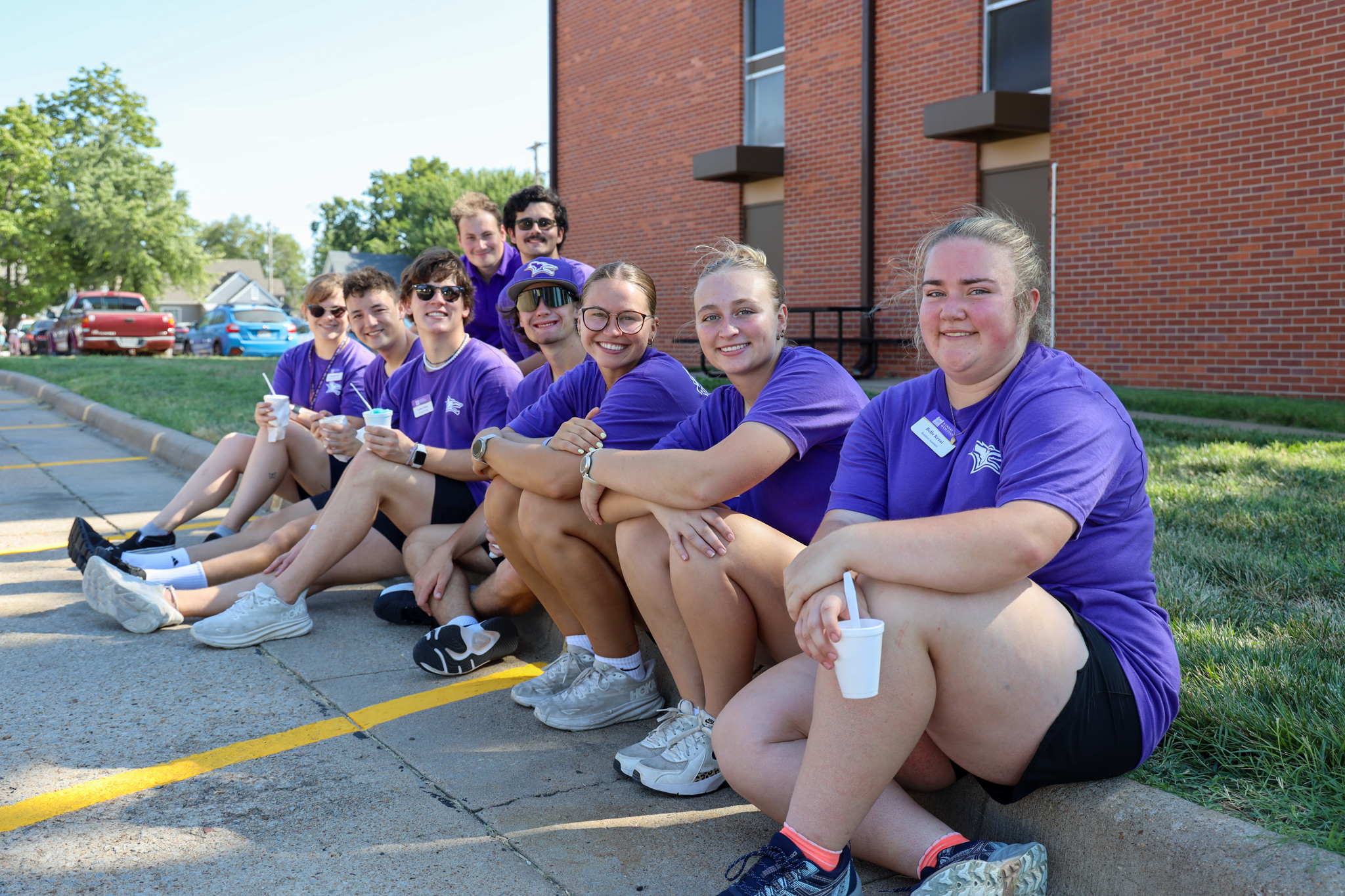 Group of students sitting on curb smiling