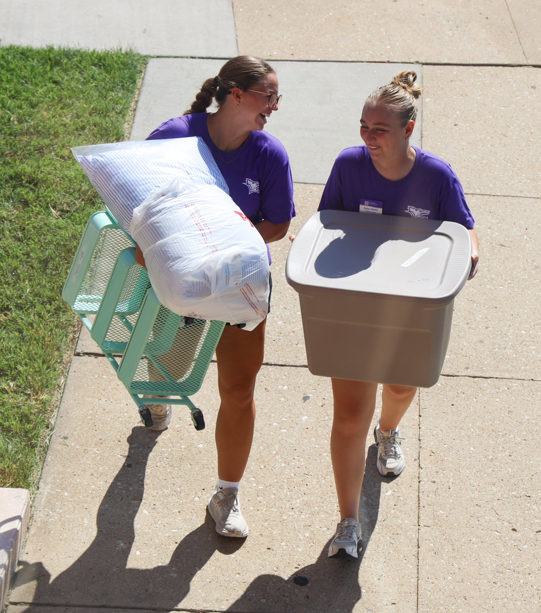 Two female students walking and carrying items