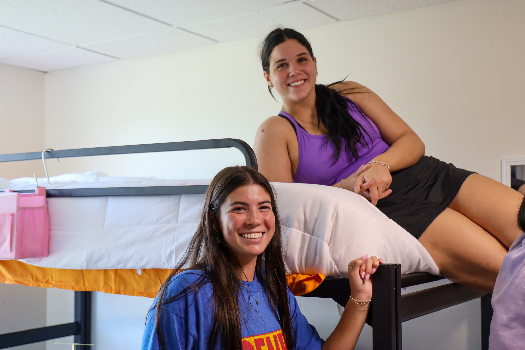 Two female students in res hall, one on bunk
