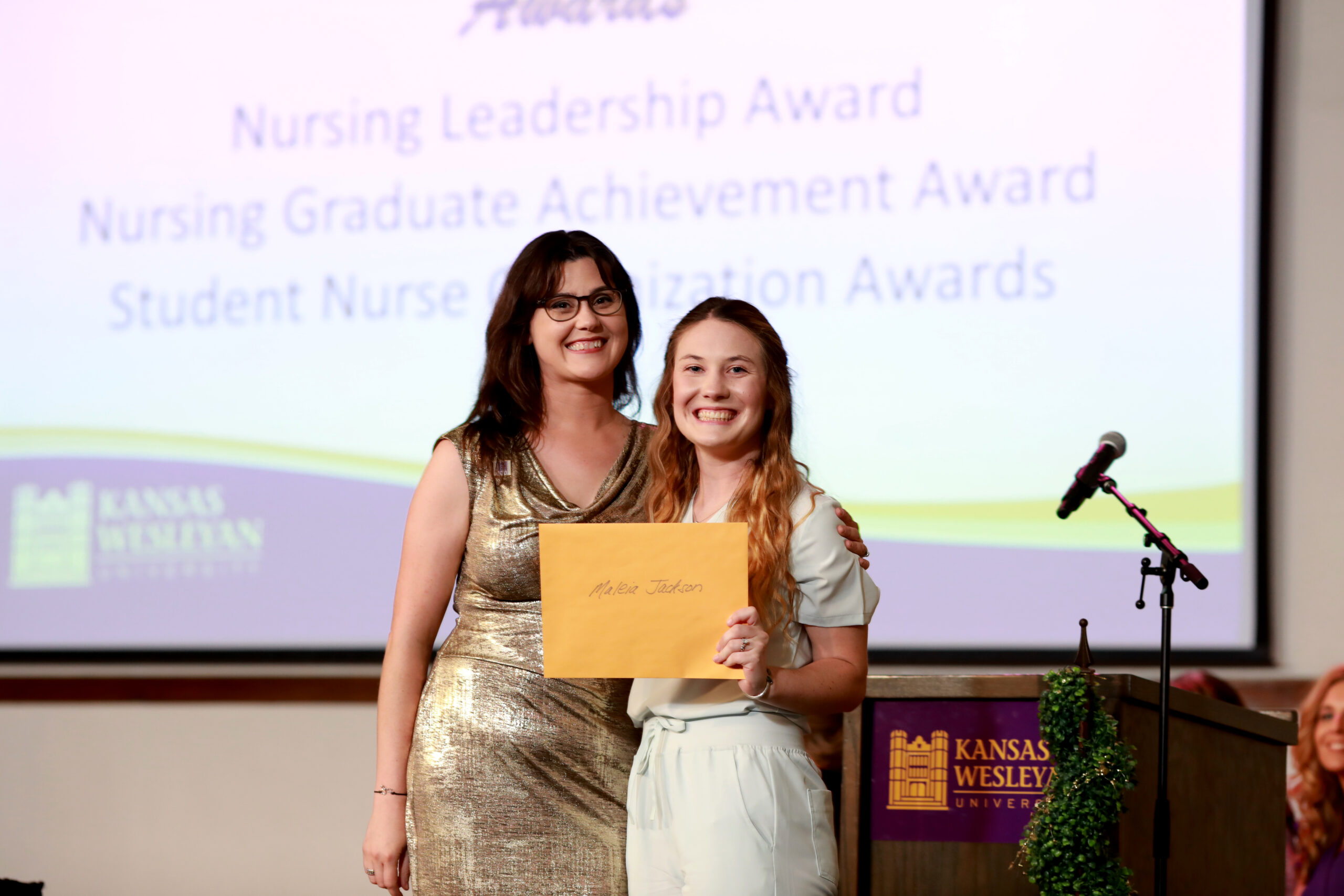 Two women on stage one giving the other an envelope