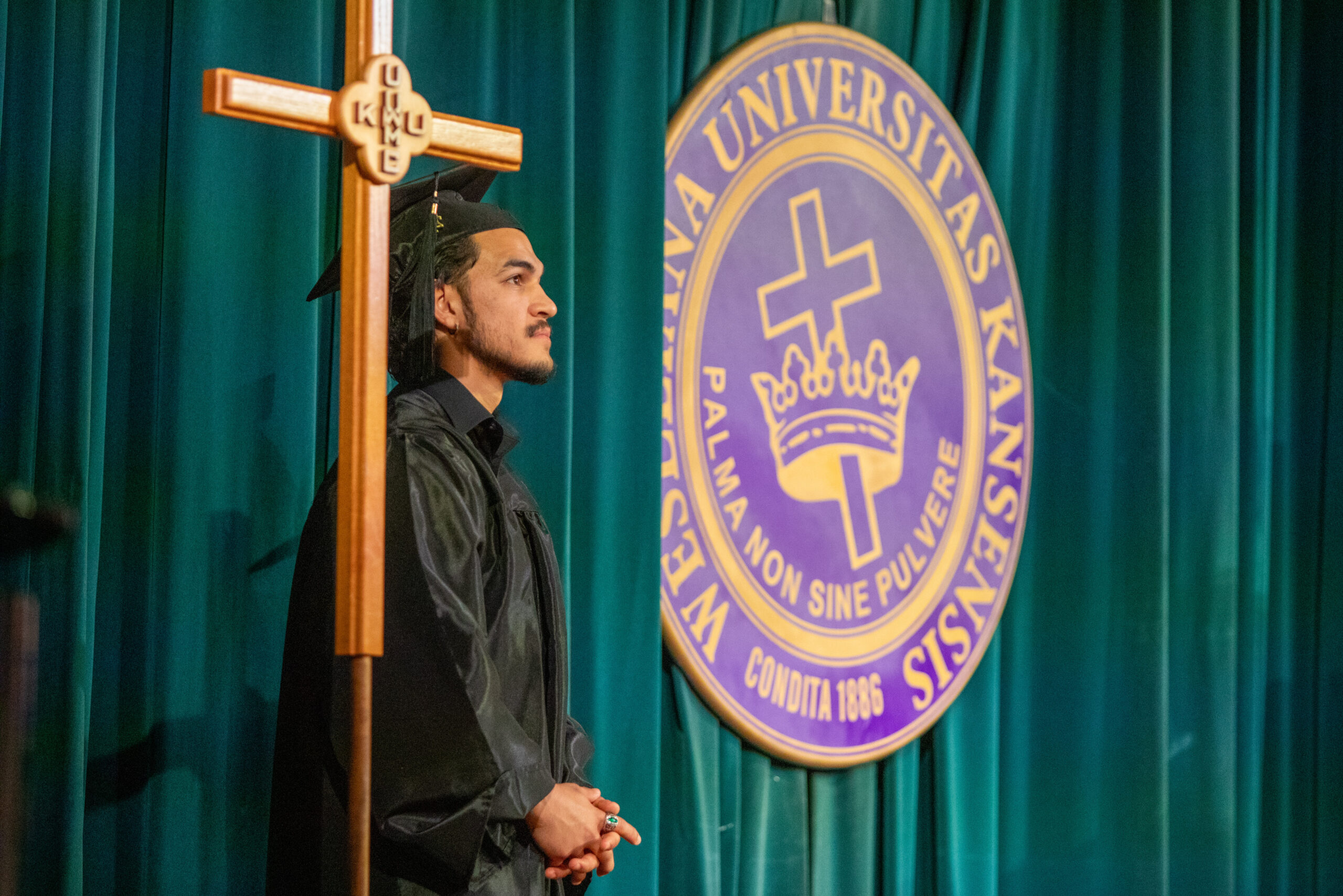 Man standing next to cross and college seal