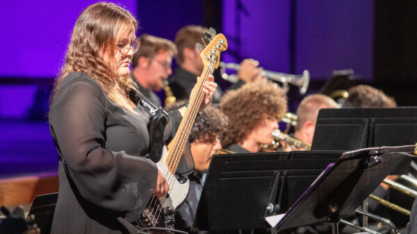 A student plays bass with other band members in the background.