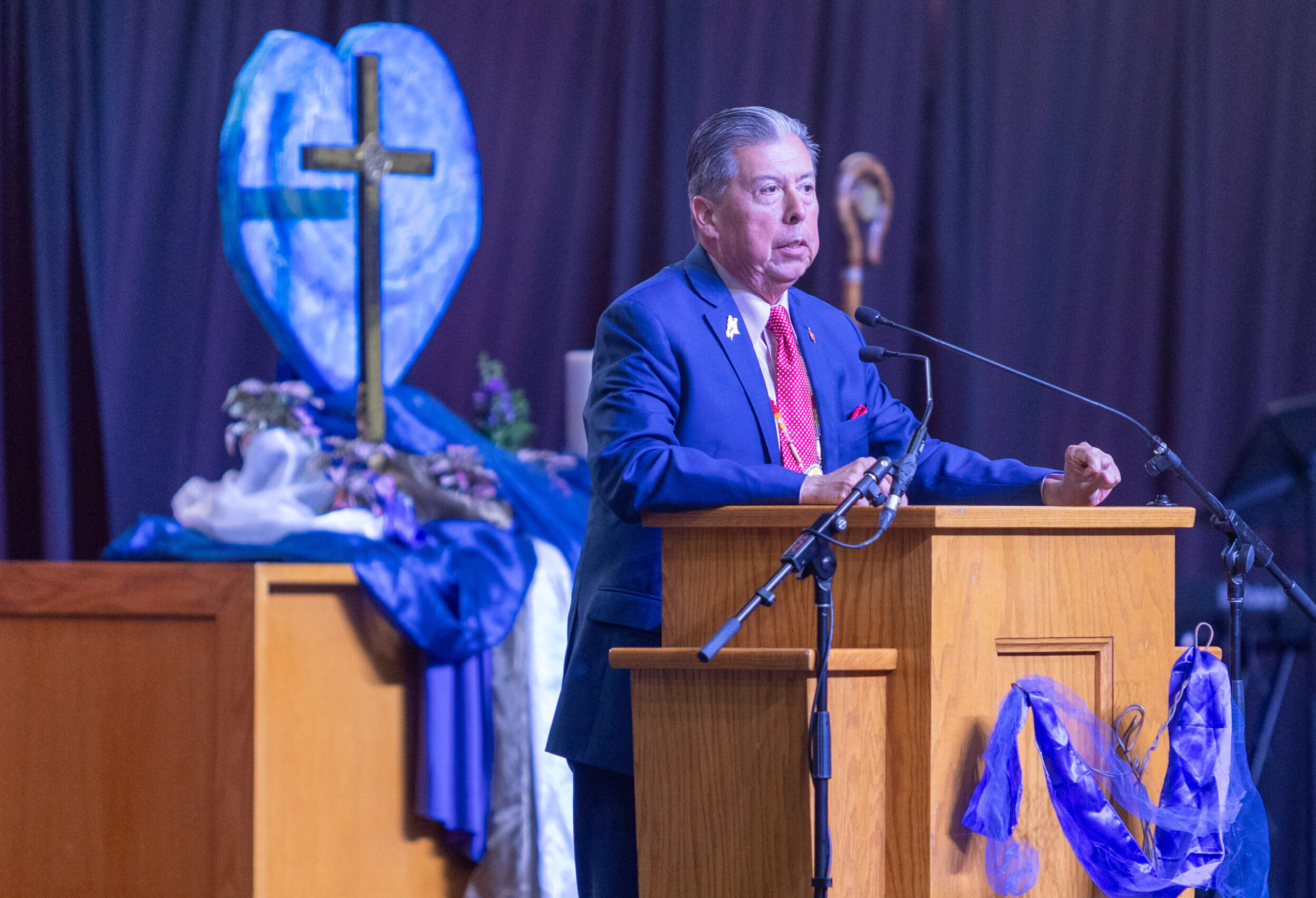Man in suit with red tie at podium speaking